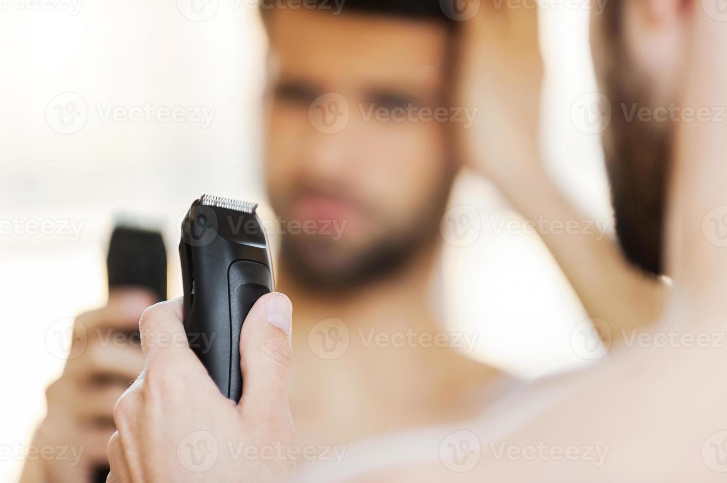 Displeased with his new shaver. Rear view of frustrated young man holding electric shaver and expressing negativity while standing in front of the mirror photo