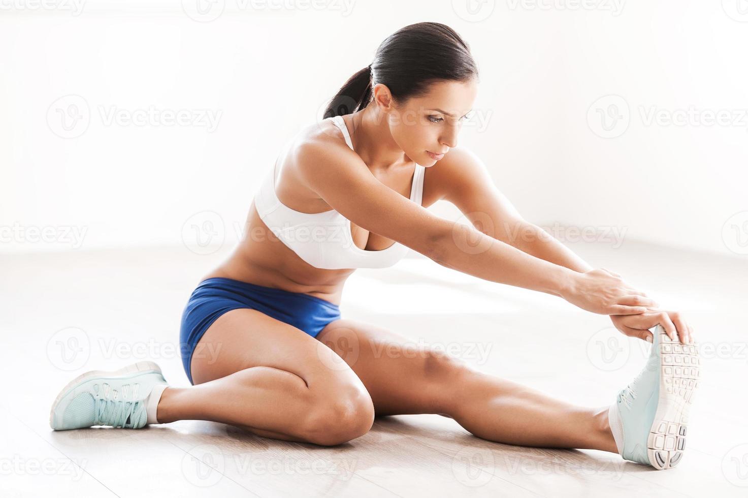 Stretch for success. Beautiful young woman in sports clothing doing stretching exercises while sitting on the floor photo