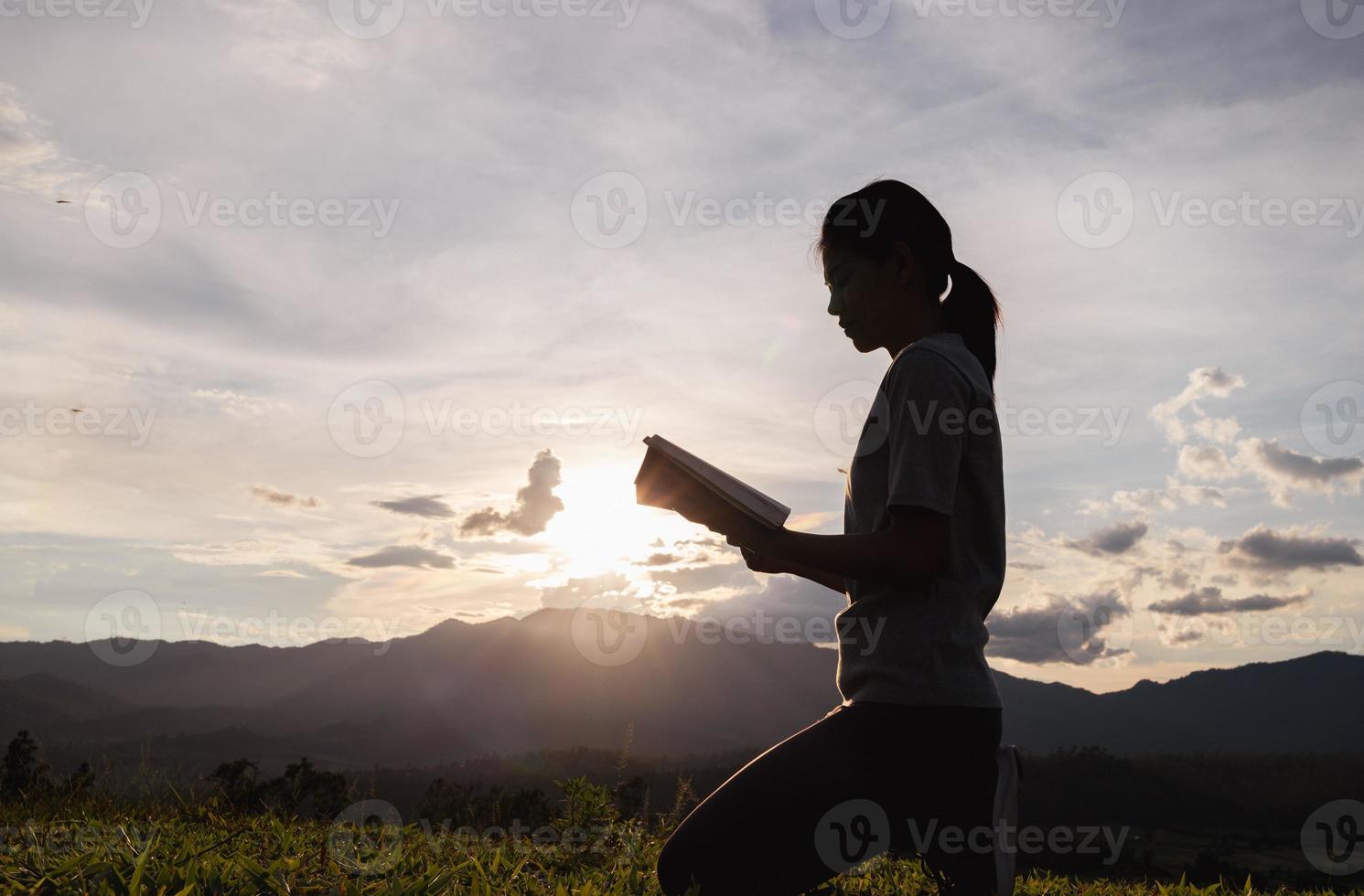 silueta de mujer rezando a dios con biblia en la montaña al fondo del atardecer. mujer levantando sus manos en adoración. concepto de religión cristiana. foto