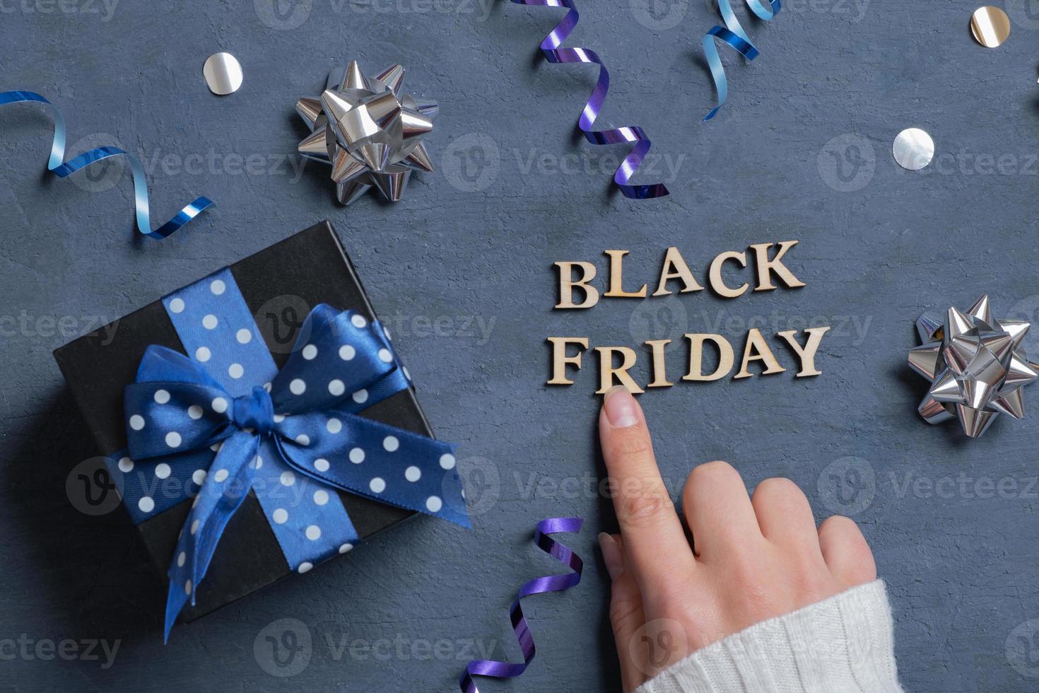 Black Friday text and female hand with gift and holiday tinsel flat lay flat lay on dark cement background. Top view photo