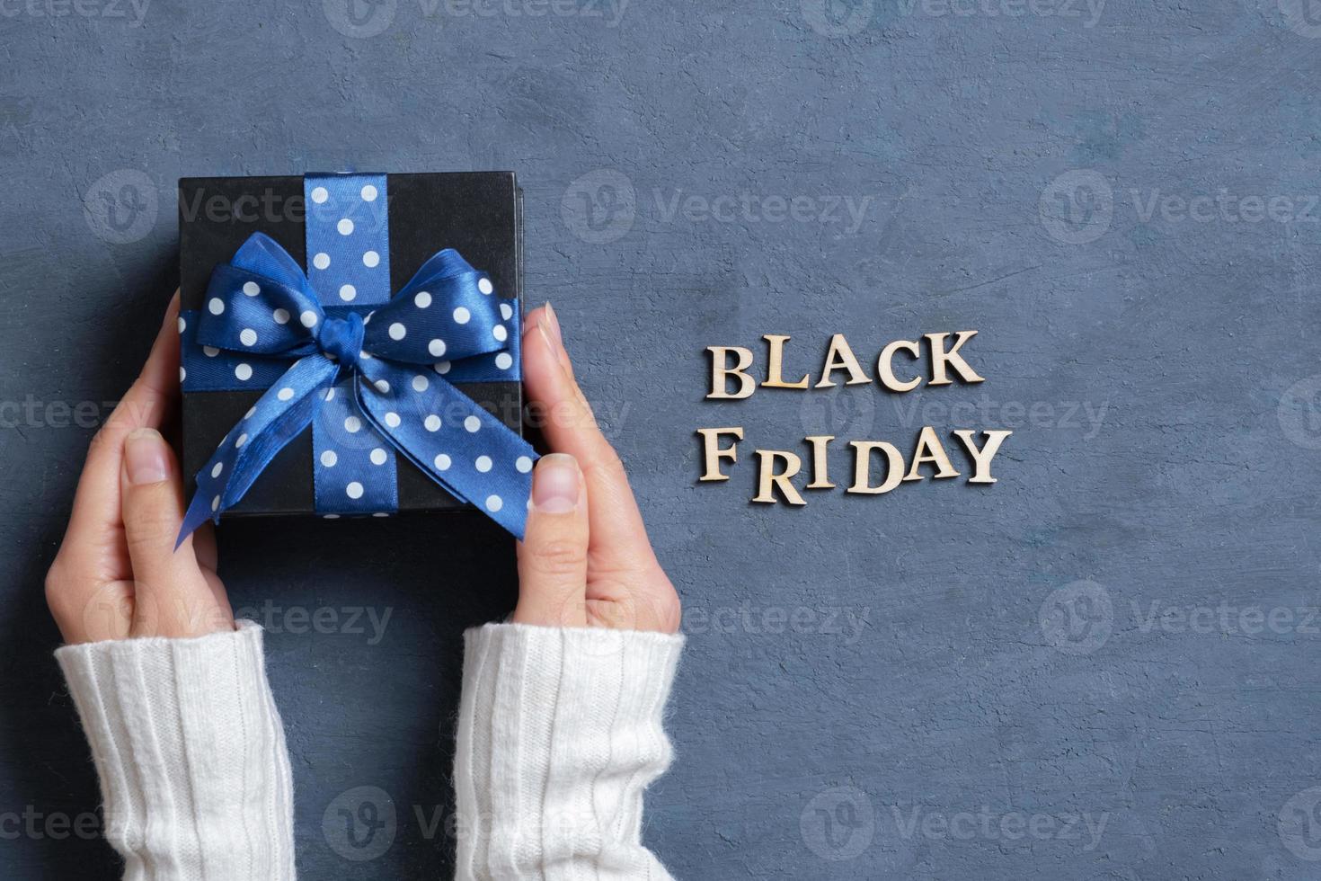Black Friday text with gift in female hands flat lay on dark cement background. Top view photo