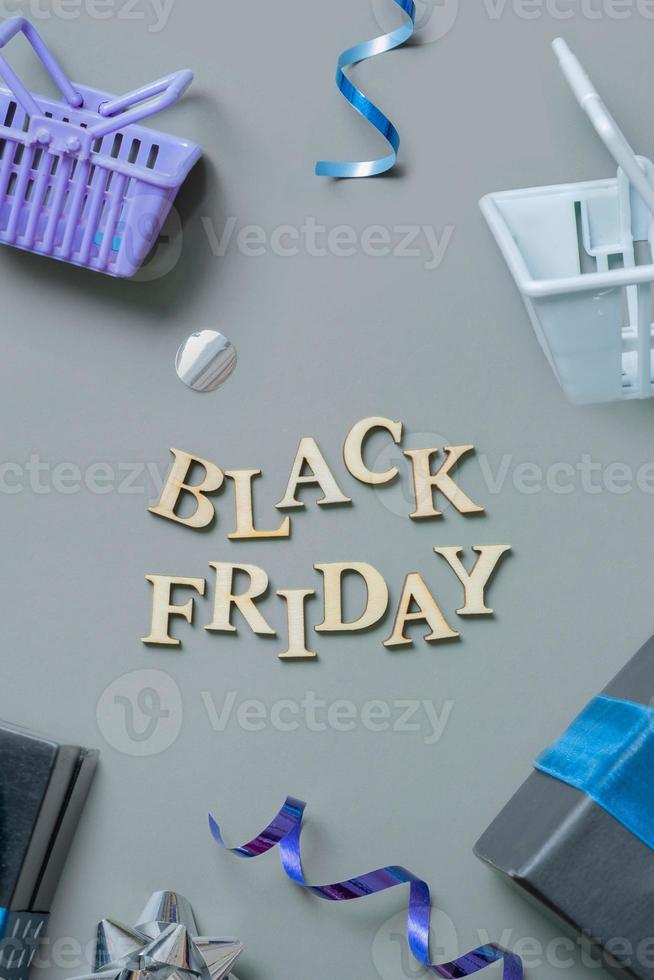 Black friday text with gifts, shopping baskets and festive tinsel flat lay. Vertical format photo