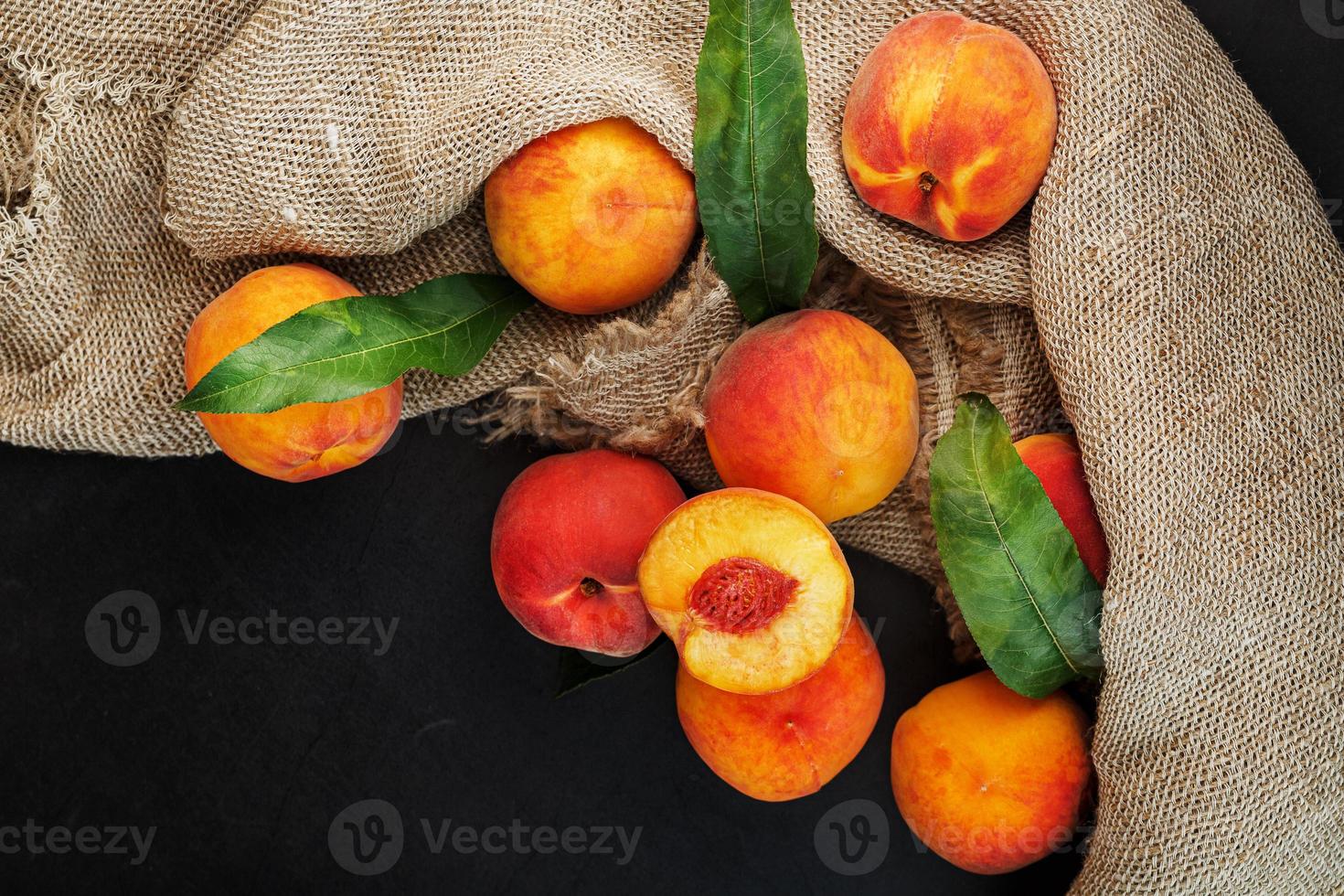 Sweet Peaches on a sharp stone table with a cloth of burlap and a slice of juicy peach with a bone. photo