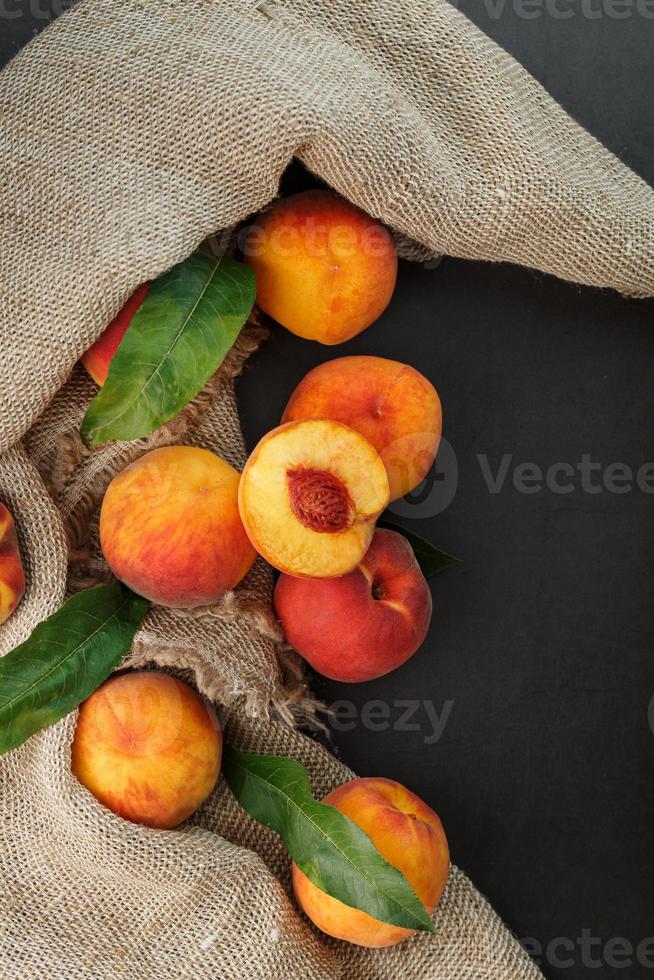 Peach fruit on a black background with a cloth of burlap and green leaves. photo