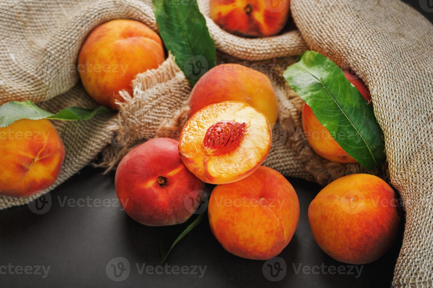 Peach fruit on a black background with a cloth of burlap and green leaves. photo