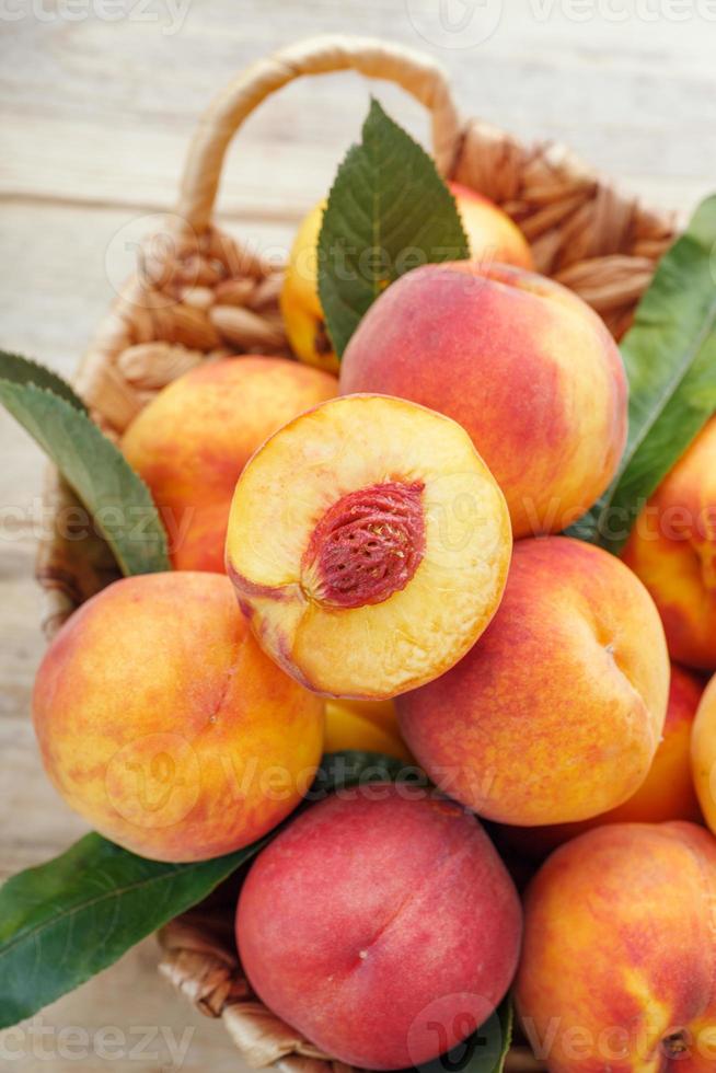 Fresh ripe peaches in a wicker basket on a wooden table, a slice of juicy peach with a stone. photo