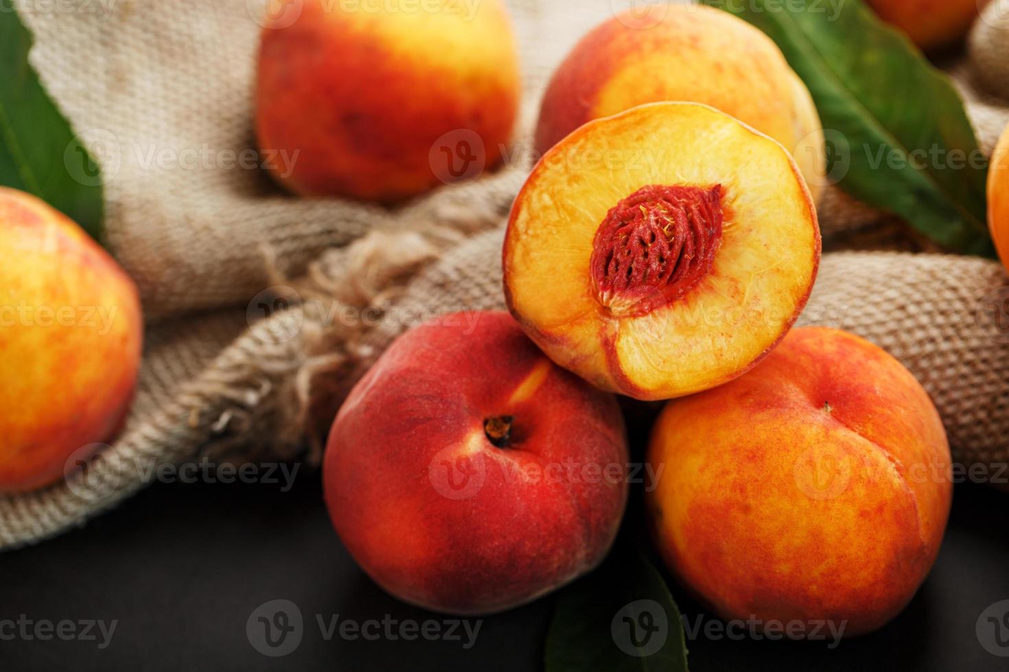 Peaches on a black background with burlap fabric and green leaves. Sweet and juicy peach slices with a stone photo