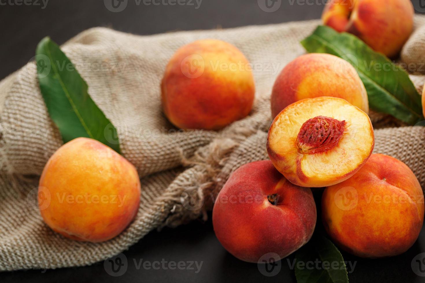 fruta de melocotón sobre un fondo negro con un paño de arpillera y hojas verdes. foto