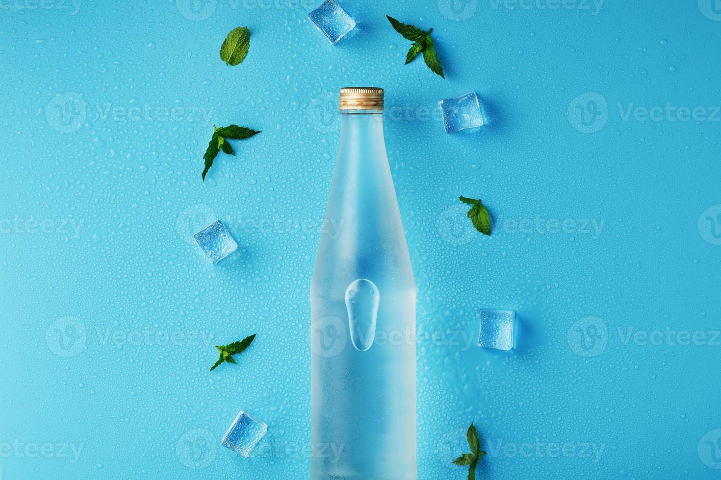 botella con una bebida helada, cubitos de hielo, gotas y hojas de menta sobre un fondo azul. foto