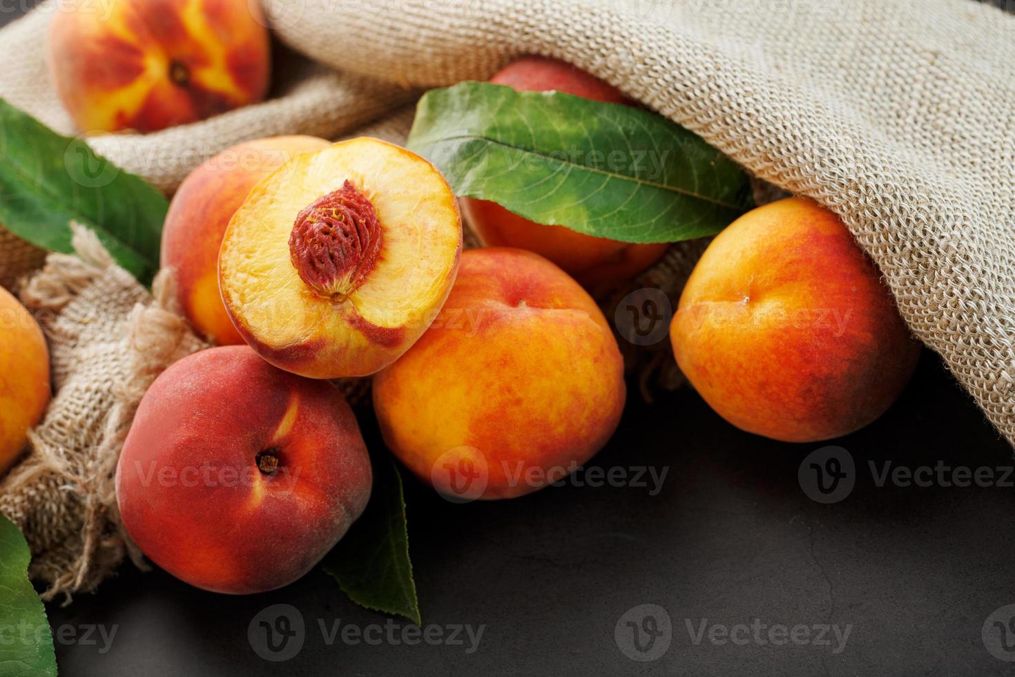 Peaches on a black background with burlap fabric and green leaves. Sweet and juicy peach slices with a stone photo