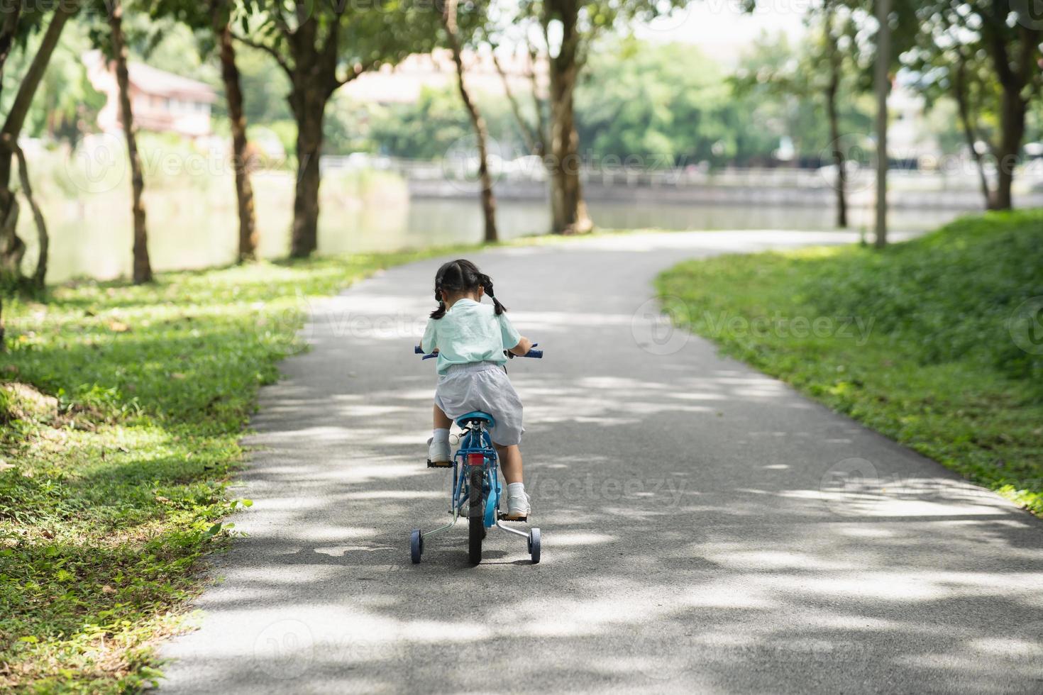 Back side view of asian baby girl child learning to ride bicycle in the park garden. Education concept for kid practiice cycling at park, baby sport concept. photo