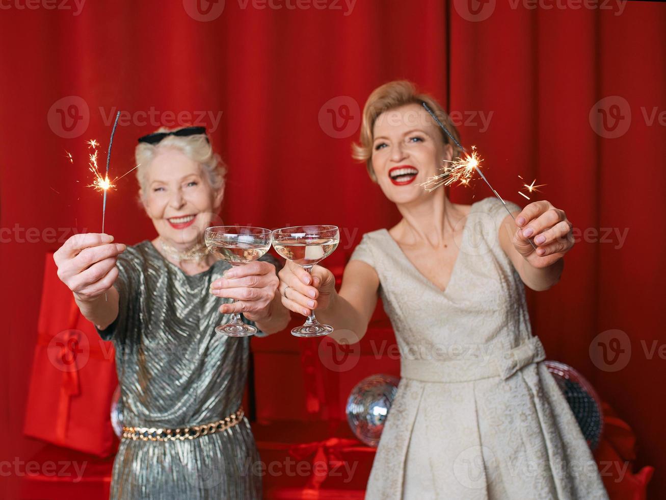 dos hermosas y elegantes mujeres mayores maduras vestidas con bengalas y gafas celebrando el año nuevo. navidad, familia, amigos, año nuevo, diversión, fiesta, estilo, concepto de celebración foto