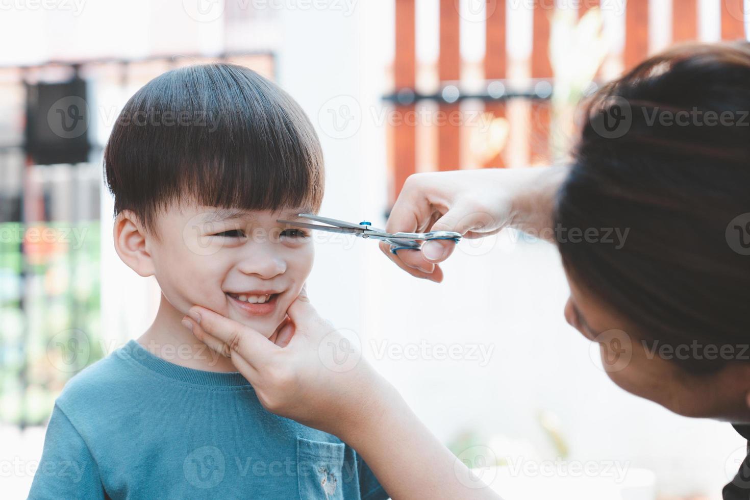 madre asiática corta el pelo de su hijo sola en casa. ideas felices de corte de pelo para niños. las madres están felices de cortar el pelo de sus hijos. foto
