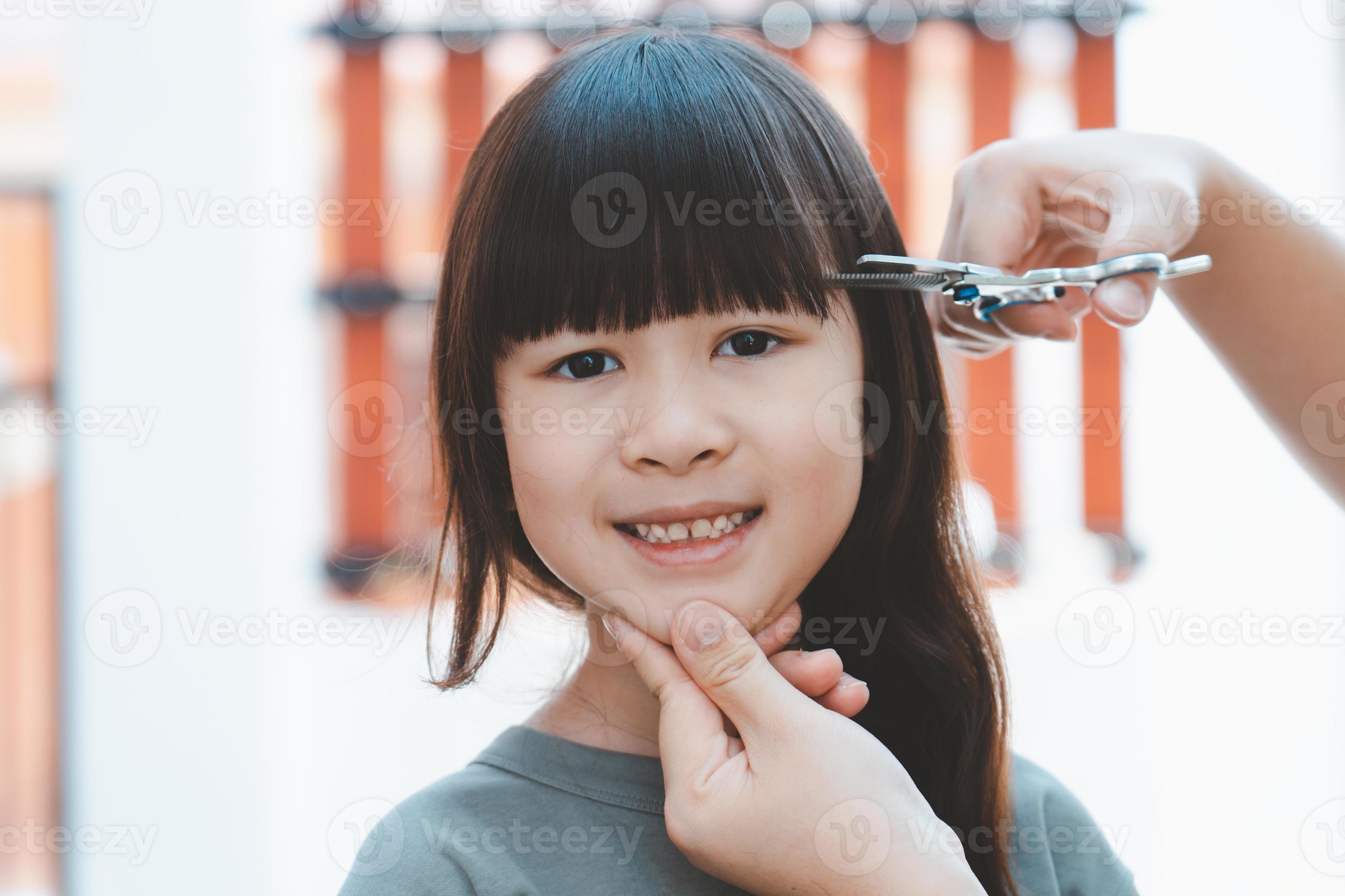 Women's hands to cut the front hair or bangs for a cute Asian girl at home.  Mothers are happy to cut their children's hair. Hair care concept 13480340  Stock Photo at Vecteezy