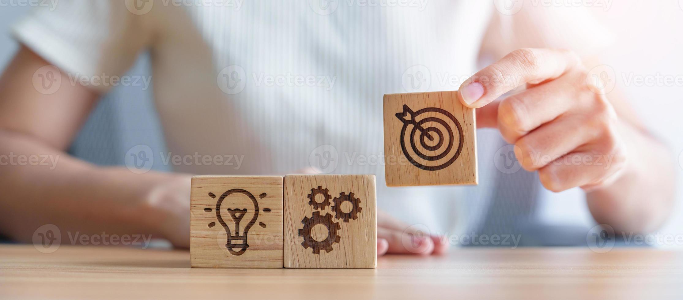 Woman hand holding dartboard above Gear and Lightbulb icon block. business planning process, goal, strategy, target, mission, action, objective, teamwork and idea concept photo