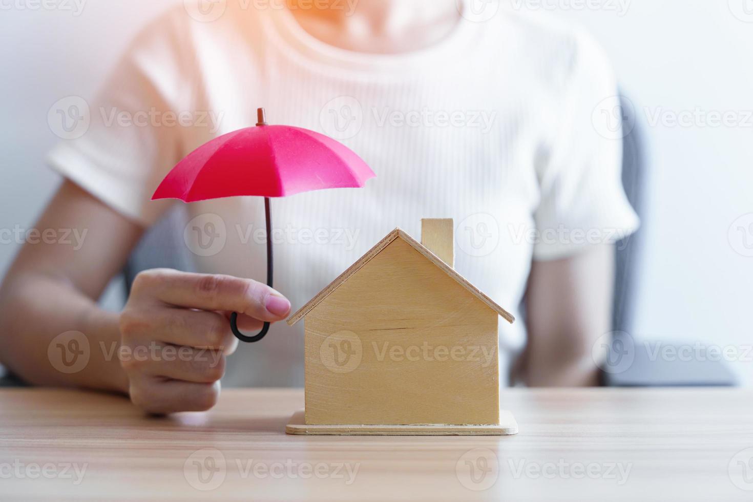 Businesswoman hand holding red Umbrella cover wooden Home model. real estate, insurance and property concepts photo