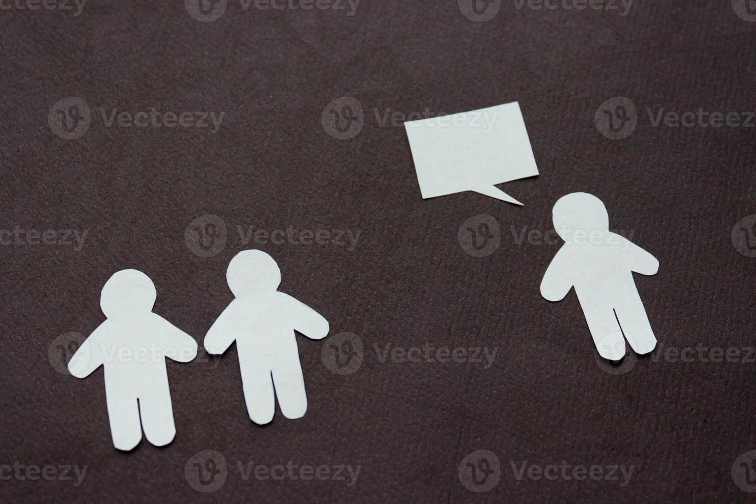 Silhouettes of people cut from white paper on a black background. A couple of people stands in front of one person who is speaking. photo