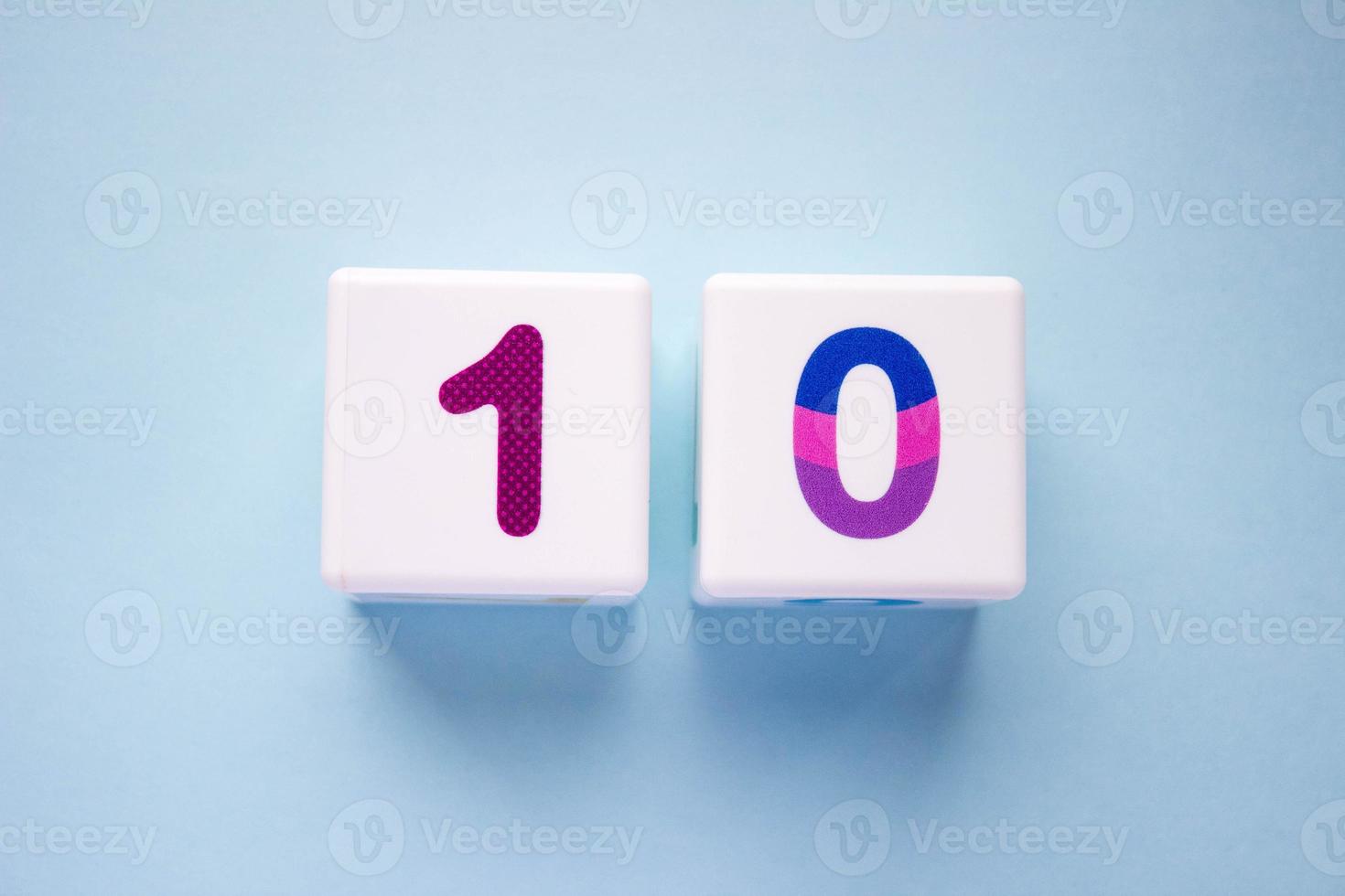 Close-up photo of a white plastic cubes with a colorful number 10 on a blue background. Object in the center of the photo
