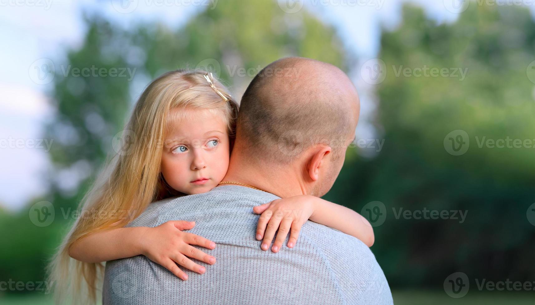 pequeña hija rubia y triste abrazando a su padre foto