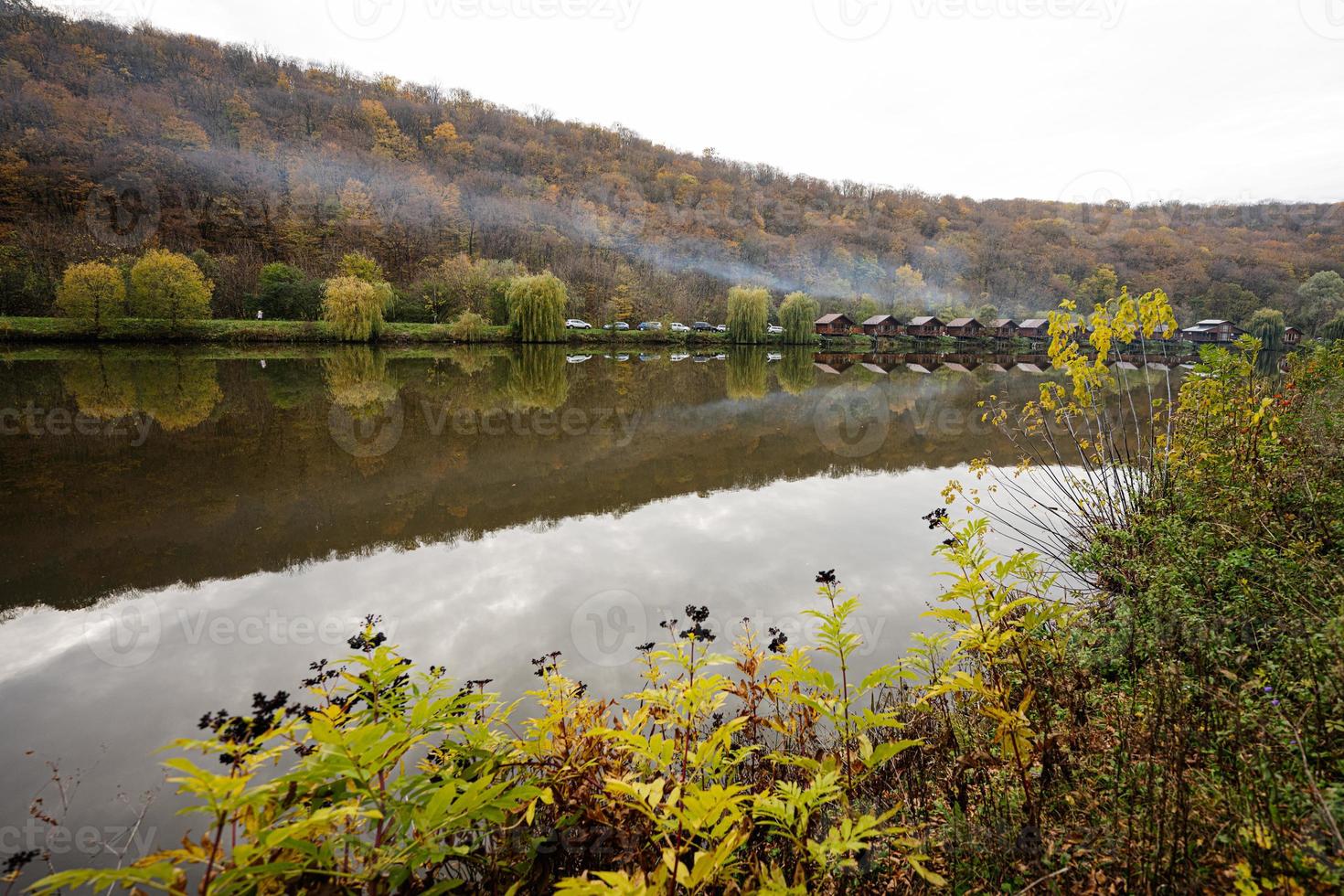 paisaje campestre. casas de madera con humo en el lago. reflejos de un edificio en el agua en un día de otoño. foto