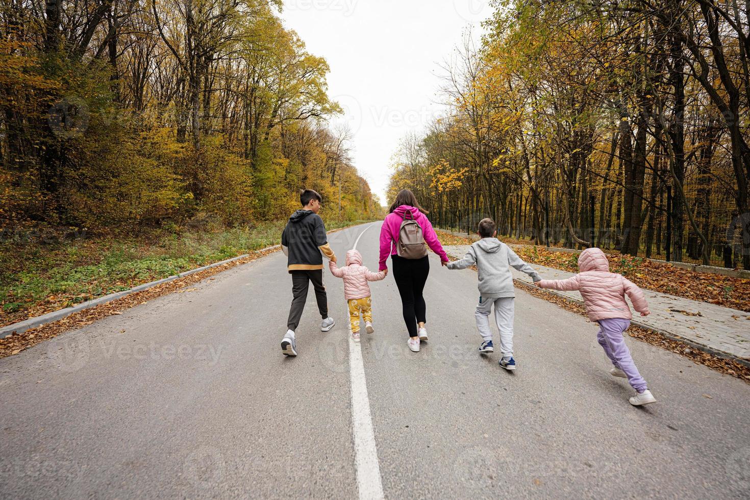 Back of mother with four kids running on road at autumn fall forest. photo