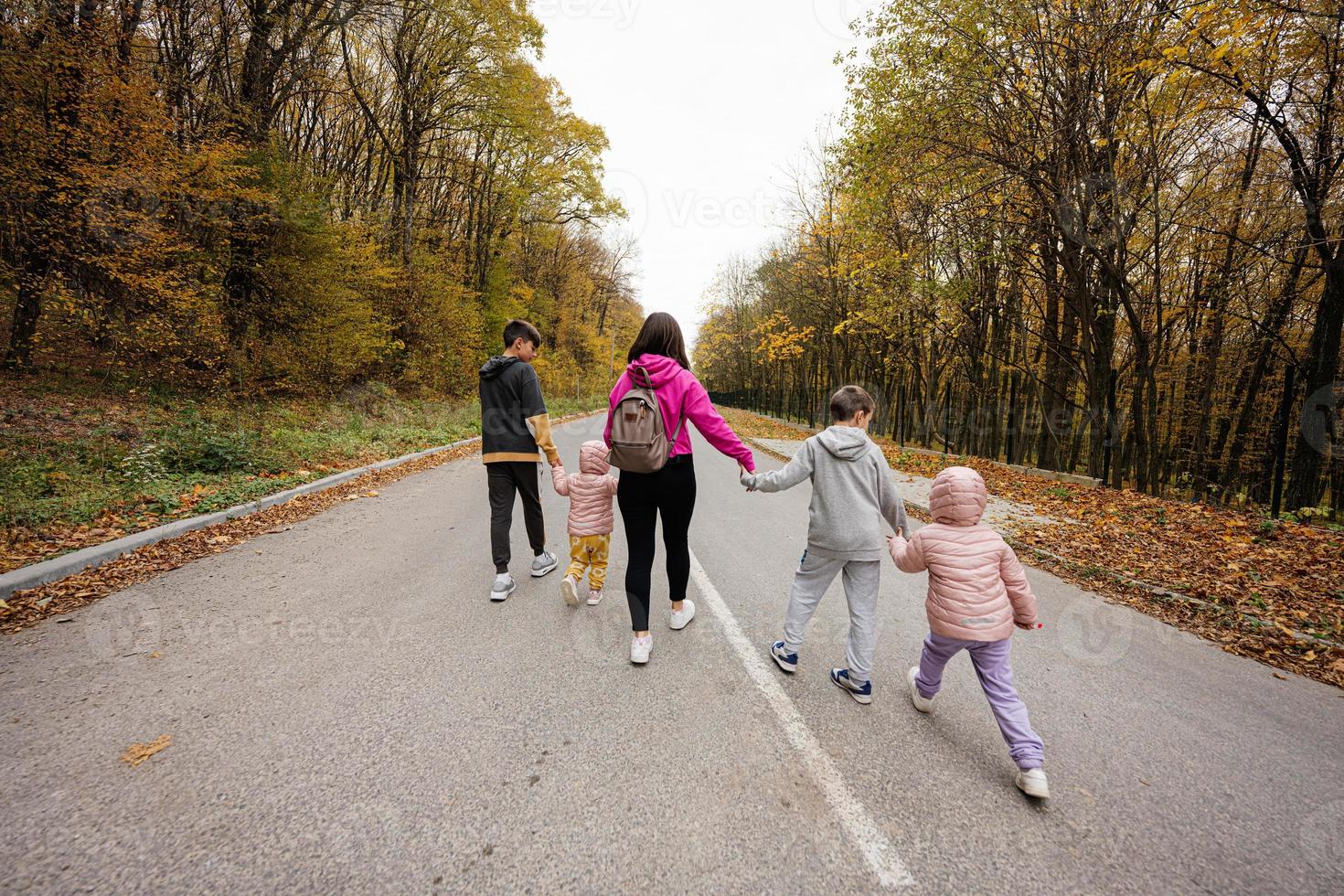 Back of mother with four kids running on road at autumn fall forest. photo