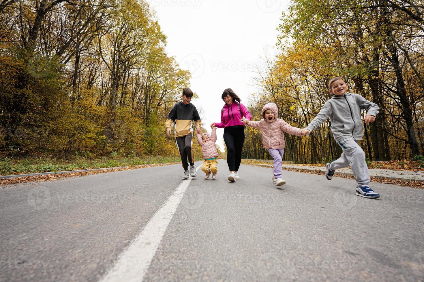 madre con cuatro hijos corriendo en la carretera en el bosque de otoño. foto
