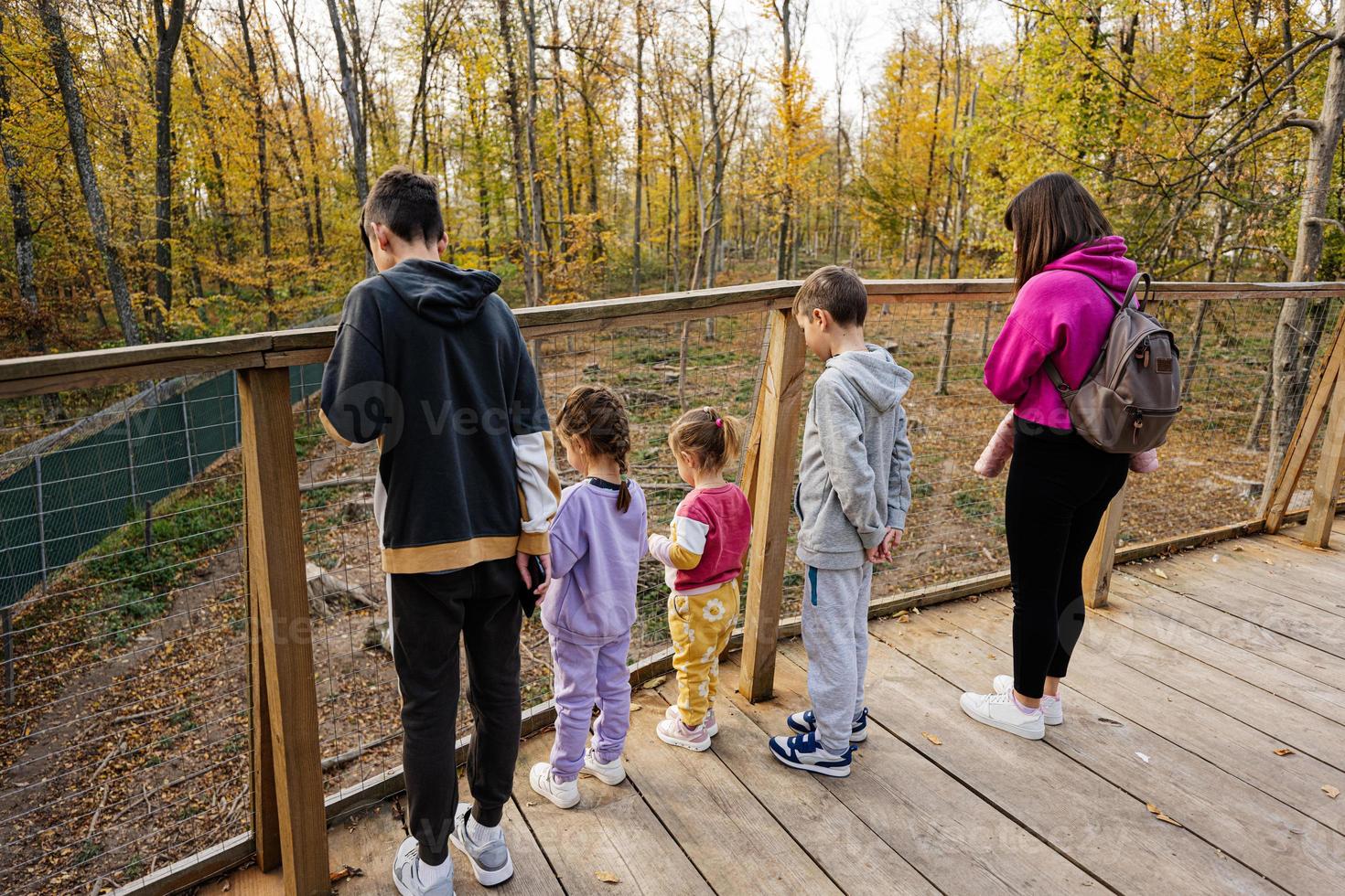 Family with four kids looking at wild animals from wooden bridge. photo