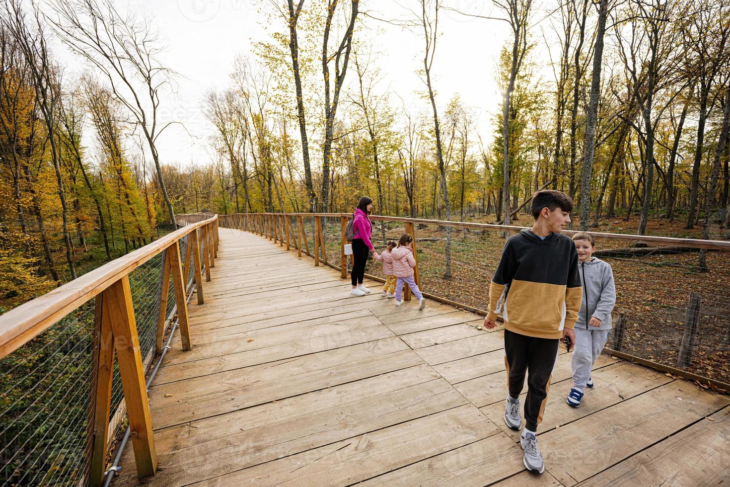 Mother with four kids walking at wooden bridge in autumn forest. photo