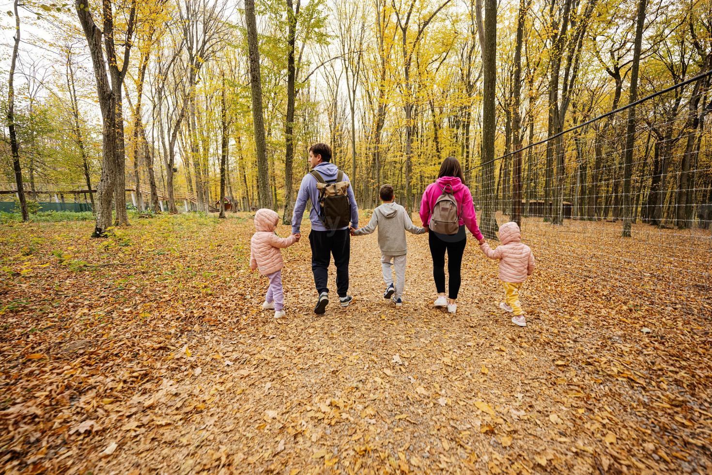 Back of family with kids on a walk in autumn forest. photo