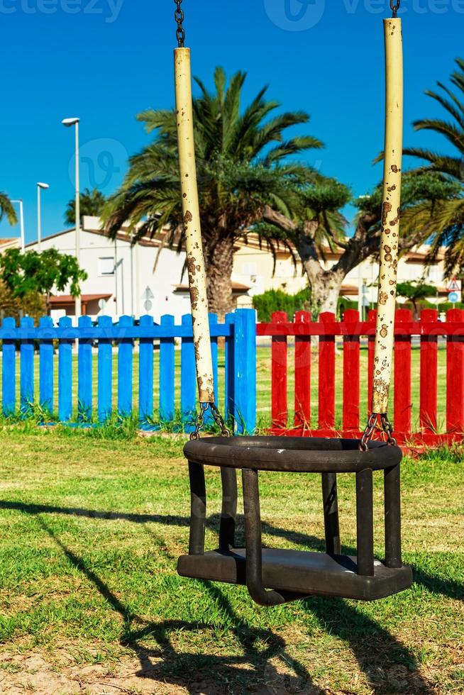 Swing in the playground with colored fences in the background. Vertical image. photo