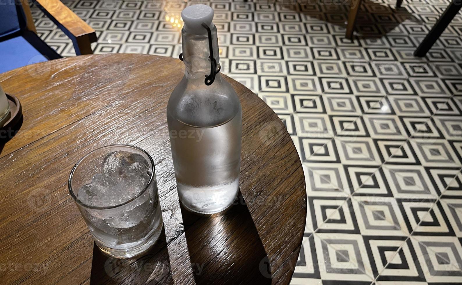 Selective focus, A clear glass filled with ice and clear glass bottle holds cold mineral water sits on wooden table photo