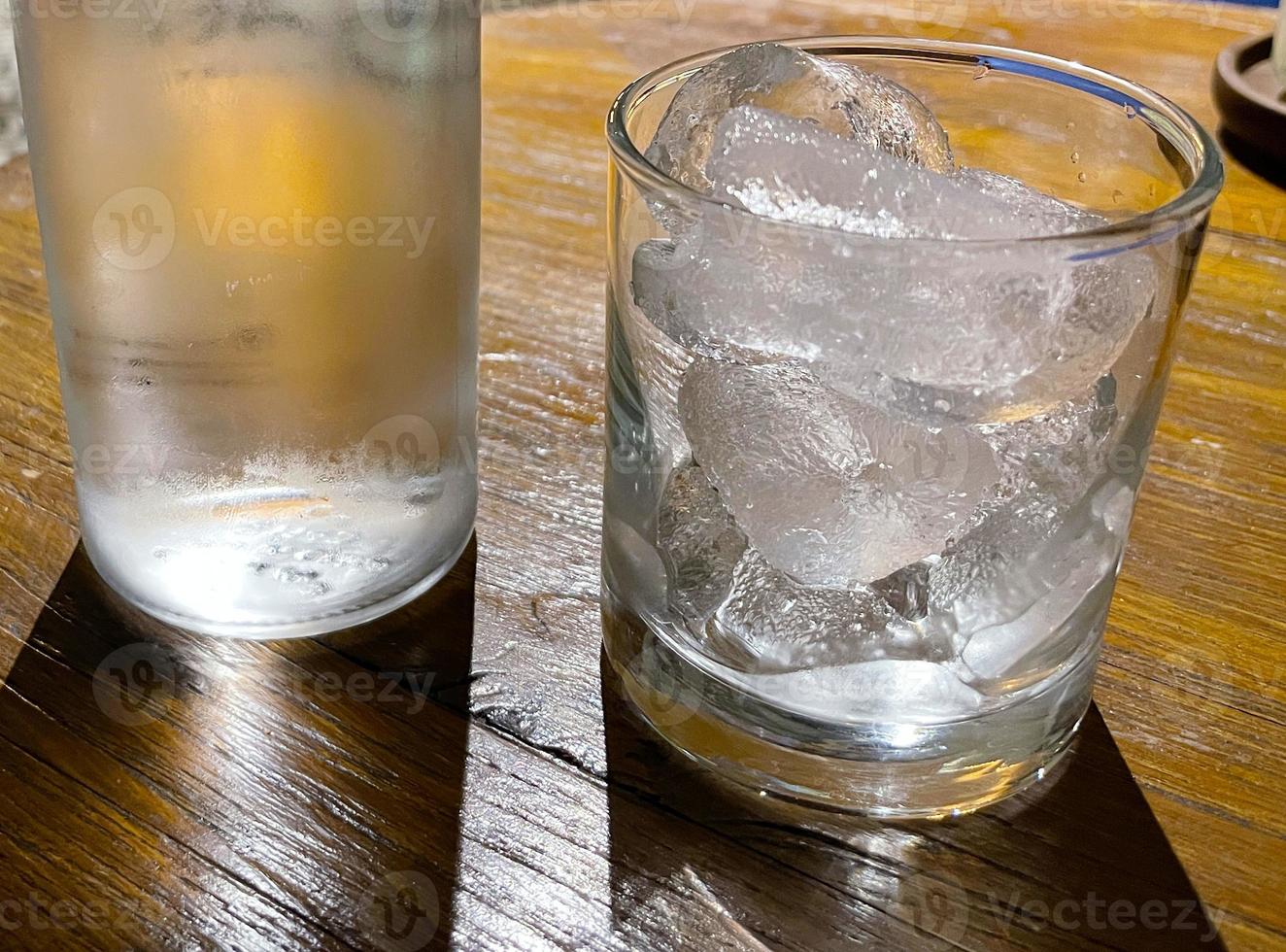 Selective focus, A clear glass filled with ice and clear glass bottle holds cold mineral water sits on wooden table photo