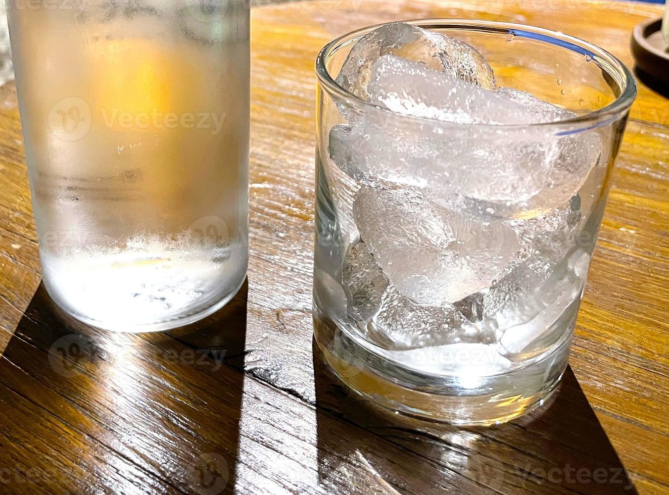 Selective focus, A clear glass filled with ice and clear glass bottle holds cold mineral water sits on wooden table photo