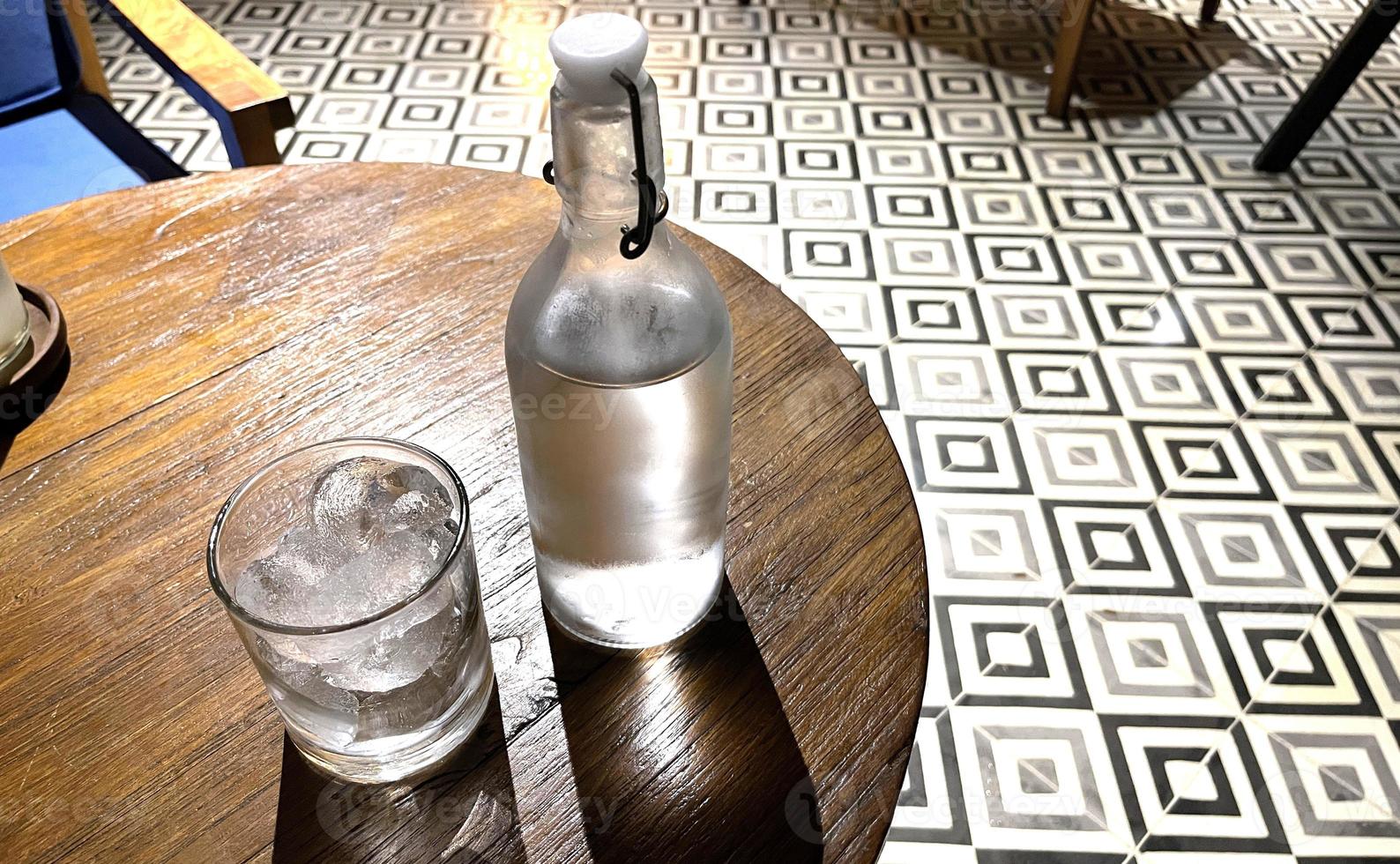 Selective focus, A clear glass filled with ice and clear glass bottle holds cold mineral water sits on wooden table photo