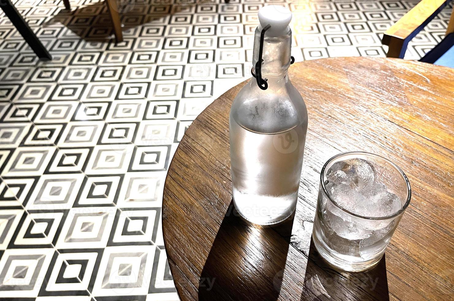 Selective focus, A clear glass filled with ice and clear glass bottle holds cold mineral water sits on wooden table photo