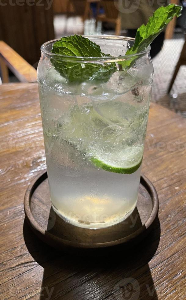 Selective focus, Delicious refreshing summer mojito with ice, lime and mint in a glass with grops. wood background photo