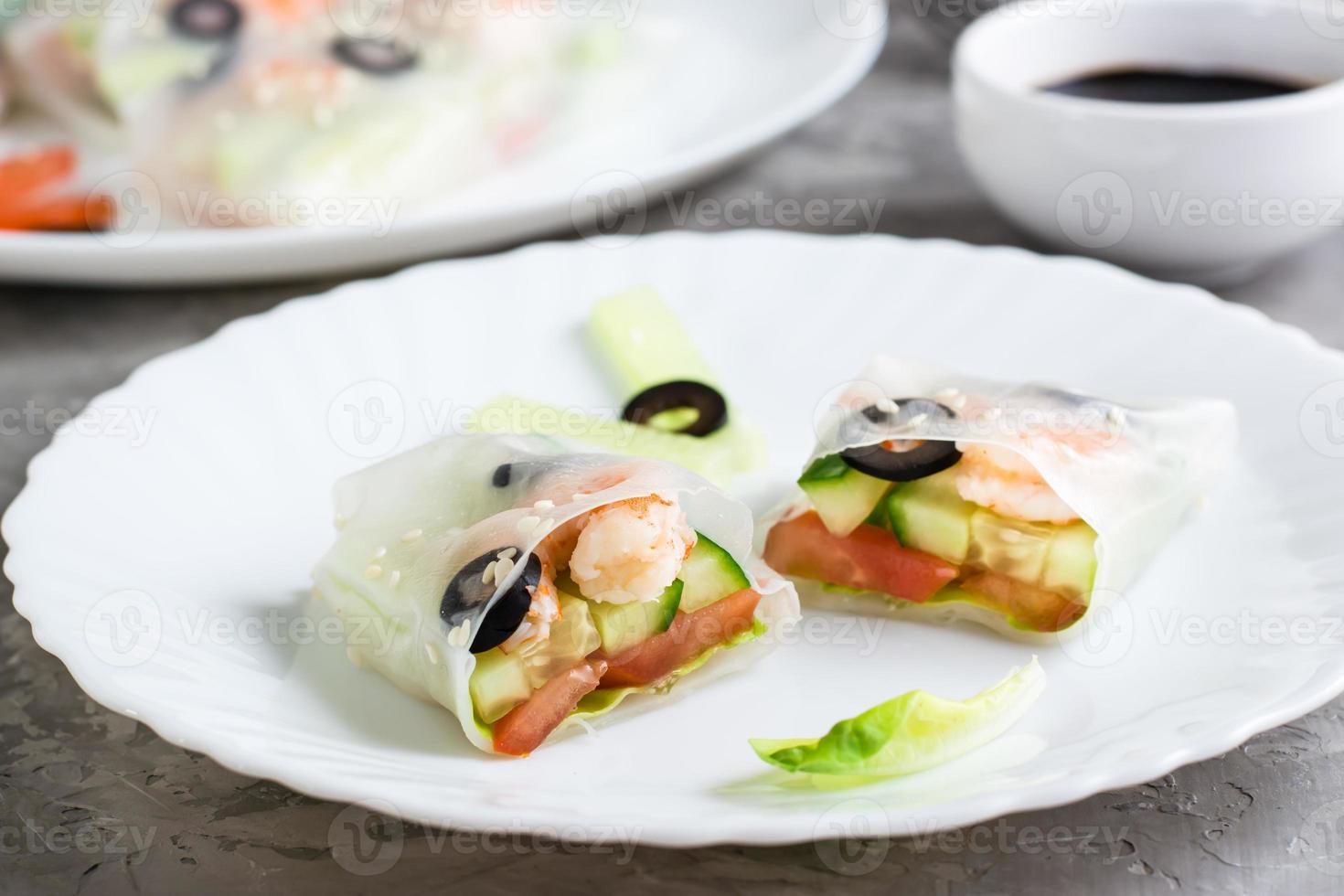 Spring roll cut in half in rice paper with seafood and vegetables on a plate on the table. Close-up photo