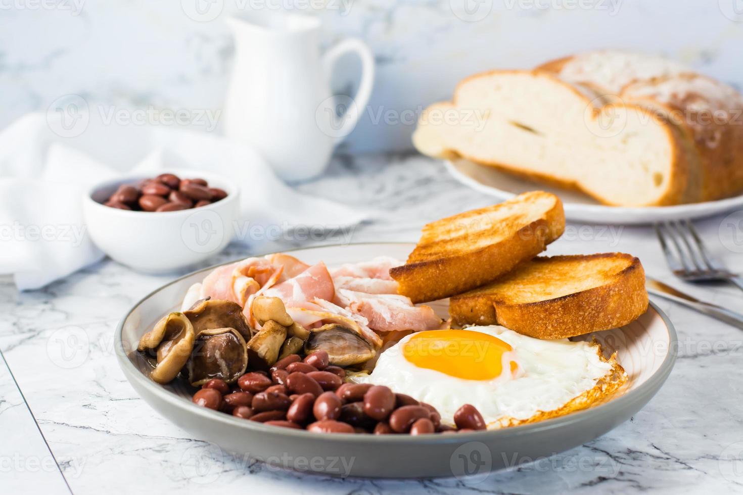 English breakfast with fried egg, bacon, beans, mushrooms and toast on a plate on the table. photo