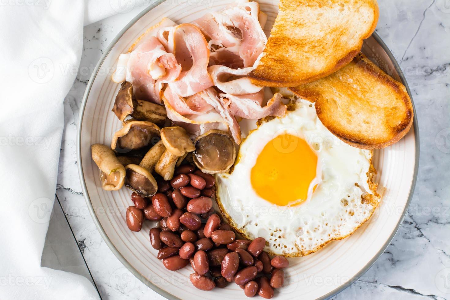 Traditional English breakfast with egg, bacon, beans, mushrooms and toast on a plate. Top view photo