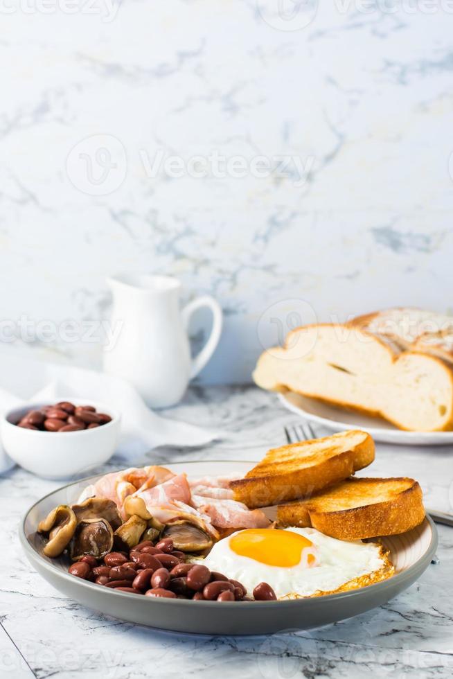Traditional English breakfast with egg, bacon, beans, mushrooms and toast on a plate. Vertical view photo