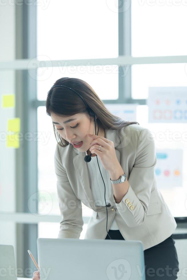 joven asiática que trabaja en un centro de llamadas consultando información sobre inversiones en acciones con clientes que piden consejo con emoción de seriedad foto