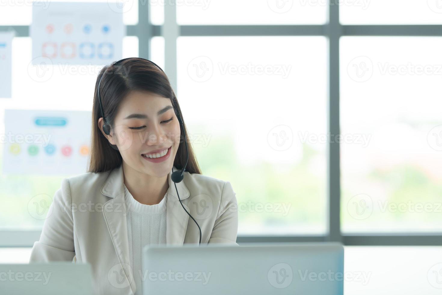 joven asiática que trabaja en un centro de llamadas consultando información sobre inversiones en acciones con clientes que piden consejo foto