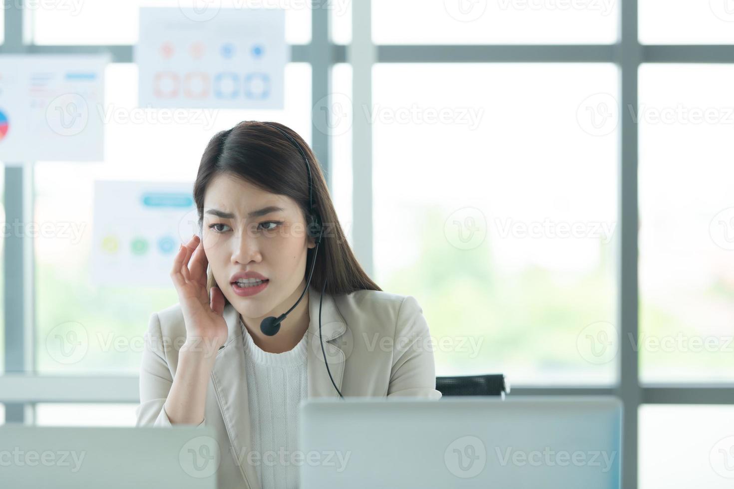 joven asiática que trabaja en un centro de llamadas consultando información sobre inversiones en acciones con clientes que piden consejo con emoción de seriedad foto