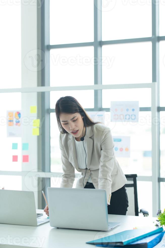 joven asiática que trabaja en un centro de llamadas consultando información sobre inversiones en acciones con clientes que piden consejo con emoción de seriedad foto