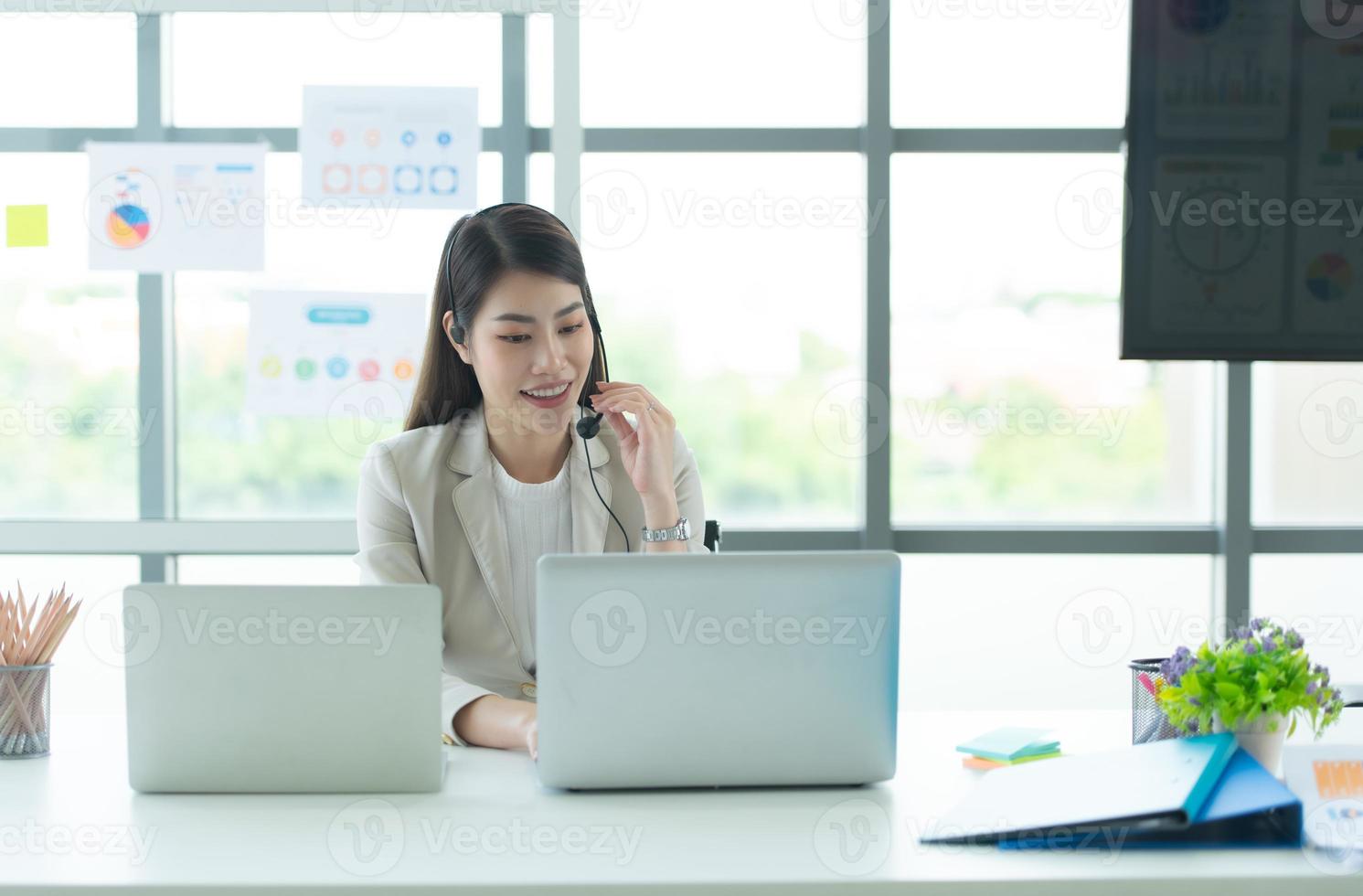 joven asiática que trabaja en un centro de llamadas consultando información sobre inversiones en acciones con clientes que piden consejo foto