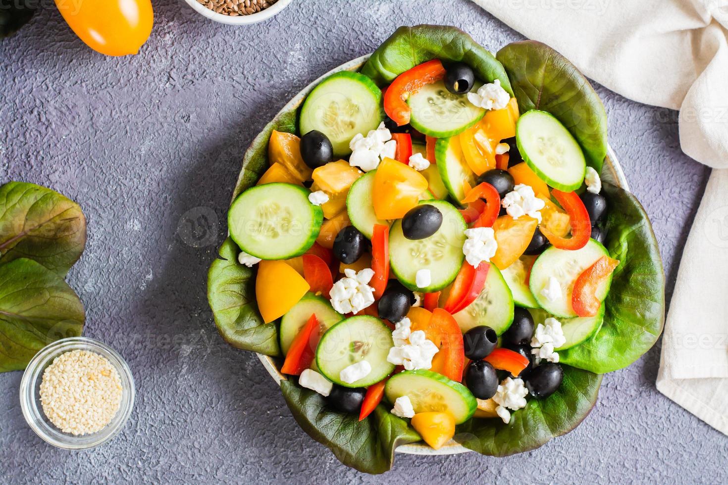 Greek salad of fresh vegetables, leaves and feta cheese on a plate on the table. Top view. Close-up photo