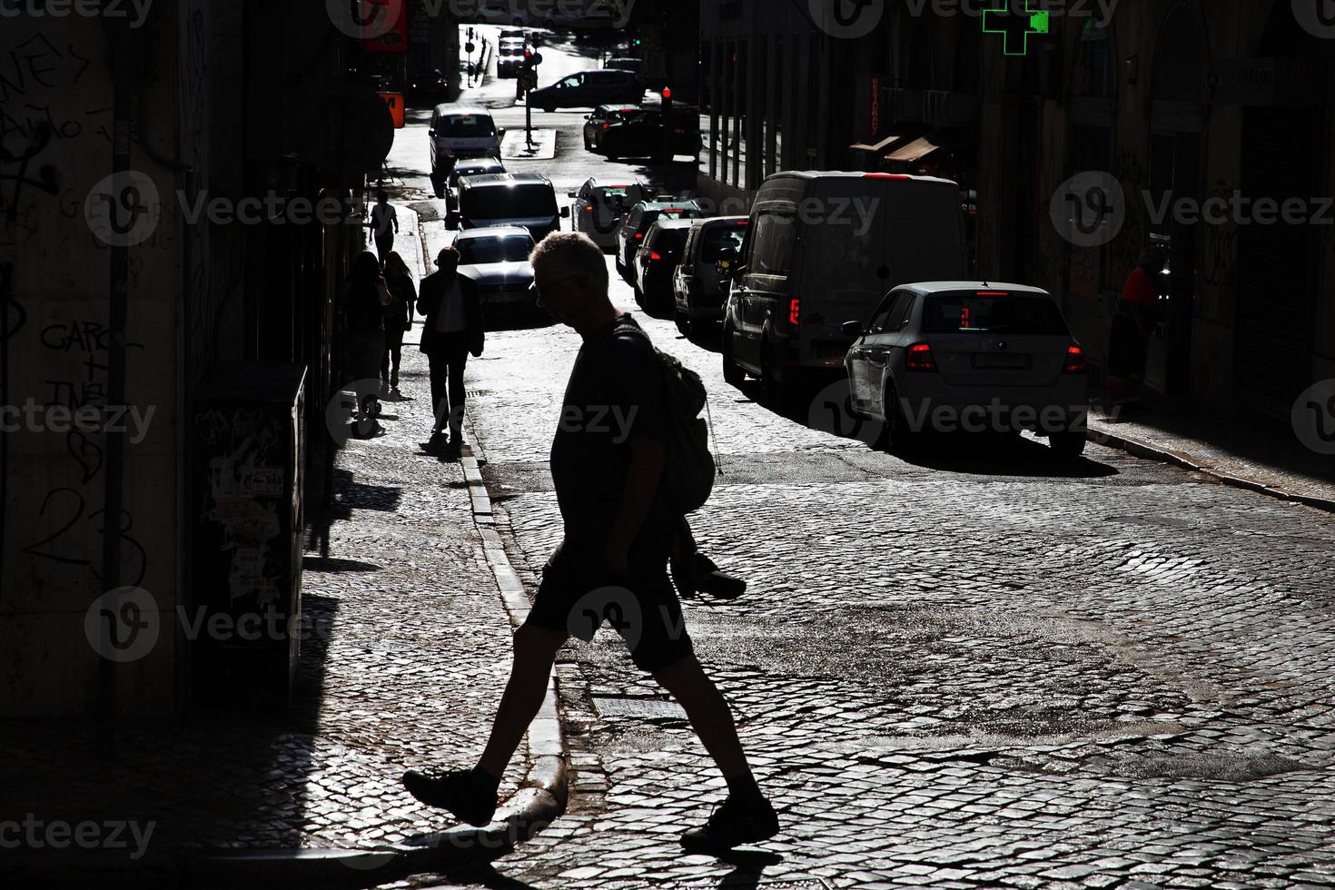 Silhouette of a man crossing a paved road on a sunny day photo