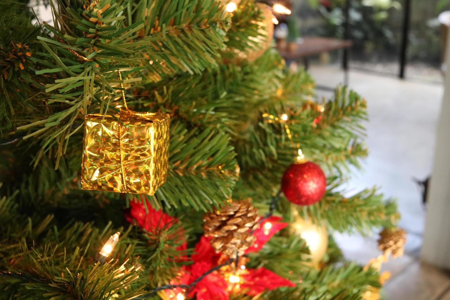 pequeña caja de regalo dorada colgada en un árbol de navidad artificial. foto