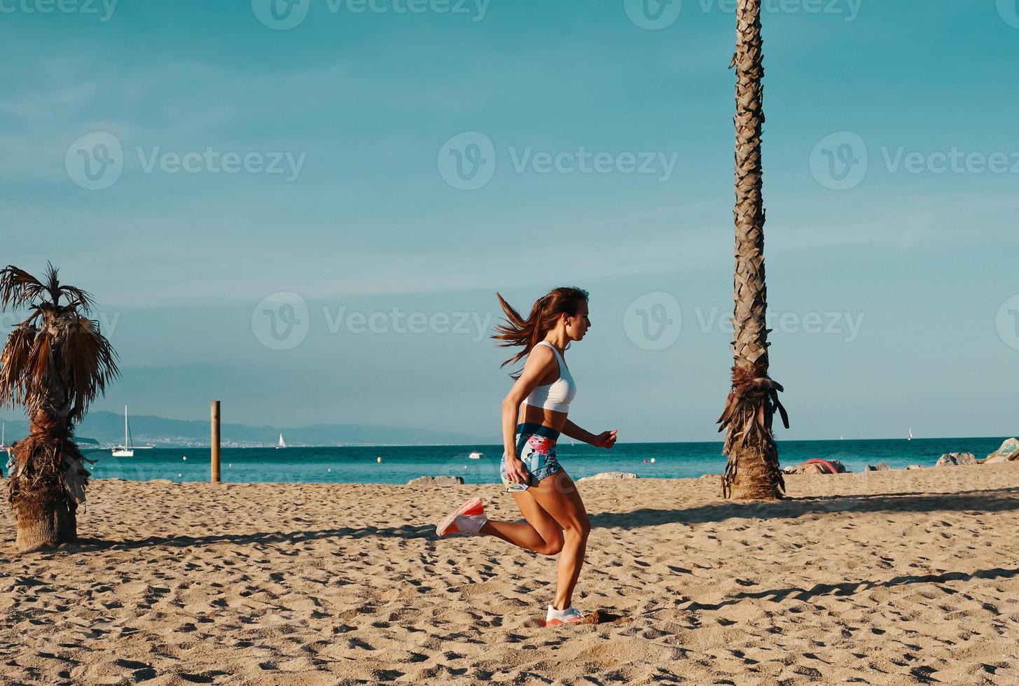 Full length of beautiful young woman in sports clothing jogging while exercising outdoors photo